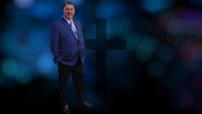 Brian Burchfield in a blue suit standing before a cross